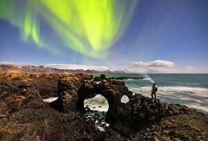 Person Collection: A man observes Gatklettur arch and northern lights, Arnarstapi, Snaefellsnes peninsula