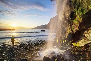 Subtropical Climate Prints: A man observes sunrise at a waterfall in Seixal black sand beach