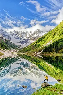 Looking At View Prints: Man photographing mountains reflected in lake with smartphone standing on rocks