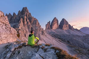 man sitting on the edge of the rocks admires the tre cime di lavaredo at sunset, Bolzano