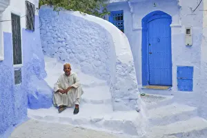 Chefchaouen Prints: Man in traditional Moroccan clothing sitting on blue painted steps, Chefchaouen