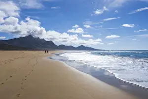 Two People Prints: Man and woman walking on golden sand of Cofete beach washed by ocean waves, Jandia