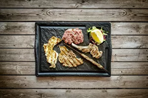 Food Gallery: Mixed grilled meat in black tray on rustic wood table background from above, Italy
