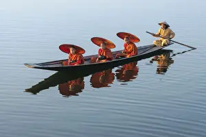 Three monks in orange robes with bowls for alms giving and a leg-rowing fisherman commute