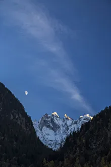 The moon on the snowy mountains illuminates the peaks at sunset Bondasca Valley The moon on the snowy mountains illuminates the peaks at sunset Bondasca Valley