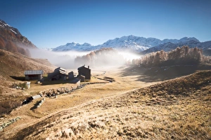 Morning fog on the mountain huts of Buaira framed by snowy peaks Sils Maloja Canton Morning fog on the mountain huts of Buaira framed by snowy peaks Sils Maloja Canton