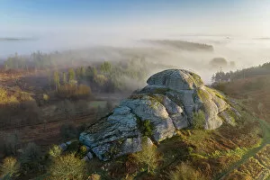 Morning mists swirl around Blackingstone Rock, a granite outcrop in Dartmoor National Park, Devon, England