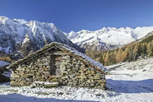 A mountain hut surrounded by snow capped peaks and colorful woods in autumn at Alp Entova