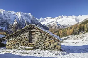 A mountain hut surrounded by snow capped peaks and colorful woods in autumn at Alp Entova