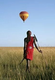 Red Ochre Collection: A Msai Warrior watches a hot air balloon float over the Mara plains