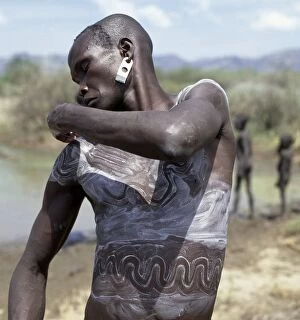 Tribesman Collection: A Mursi man smears his body with a mixture of local