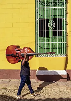 Musician with his double bass walking through the colourful street of Trinidad