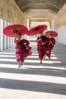 Umbrella Gallery: Myanmar, Mandalay division, Bagan. Three novice monks running with red umbrellas in a walkway