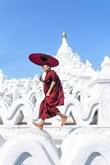 Myanmar, Mandalay division, Mingun. Novice monk with red umbrella jumping on Hsinbyume Pagoda