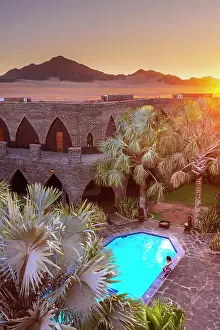 Namibian Prints: Namibia, a swimming pool in a luxury hotel in the Namib Naukluft National Park with the sun setting on the Namib desert