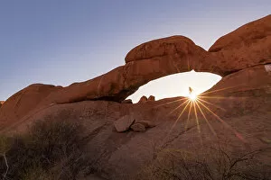 Images Dated 24th February 2023: Namibia, a woman hiking to the top of Spitzkoppe natural rock arch and looking at the sun setting MR