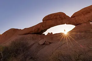 Namibian Prints: Namibia, a woman hiking to the top of Spitzkoppe natural rock arch and looking at the sun setting MR