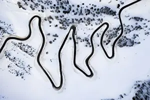 Road Trip Prints: Narrow bends of icy road along the snow capped mountain pass from above, Dolomites, Italy