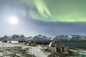 The Northern Lights and moon illuminate the glass igloos framed by icy sea Djupvik Lyngen Alps Tromso Norway Europe