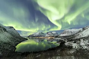Northern lights and stars light up the snowy peaks reflected in the cold sea Bergsbotn