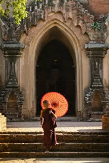 Umbrella Gallery: Novice Buddhist monk with red umbrella walking away from temple, Bagan, Mandalay Region