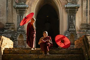 Two novice Buddhist monks with red umbrellas reading by temple, Bagan, Mandalay Region Two novice Buddhist monks with red umbrellas reading by temple, Bagan, Mandalay Region