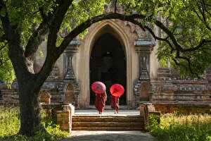 Religious Place Collection: Two novice Buddhist monks with red umbrellas walking to temple, Bagan, Mandalay Region
