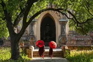 Two novice Buddhist monks with red umbrellas walking to temple, Bagan, Mandalay Region