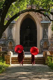 Two novice Buddhist monks with red umbrellas walking to temple, Bagan, Mandalay Region