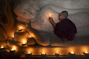 Southeast Asian Collection: A novice monk holding a burning candle while praying by Buddha statue, UNESCO, Bagan