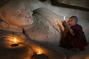 Images Dated 9th May 2020: A novice monk holding a burning candle while praying by Buddha statue, UNESCO, Bagan