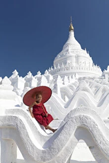 Myanmar Gallery: Novice monk sits on the white wall of Hsinbyume Pagoda holding a red umbrella, Mingun