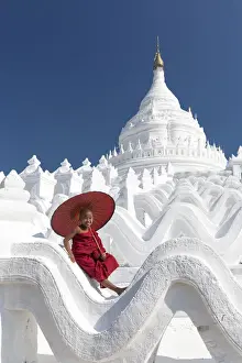 Burmese Prints: Novice monk sits on the white wall of Hsinbyume Pagoda holding a red umbrella, Mingun