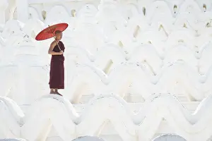 Novice monk with an umbrella standing at white Hsinbyume pagoda