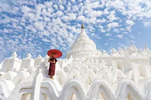 Novice monk with an umbrella standing at white Hsinbyume pagoda