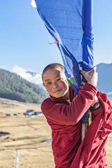 Bhutan Prints: Novice Monks(Child Monk) standing next to a prayer flag in Phobjikha Valley, Bhutan
