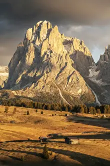 Two old cabins lost in the meadows of the Alpe di Siusi (Seiser Alm) during an early autumn sunset, with the Sassolungo and Sassopiatto in the background. Dolomites, Italy