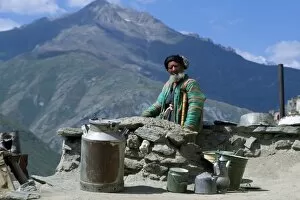 Aging Gallery: An old man sits beside the dusty road with his pots and milk churn, at Nometkun