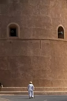Oman Collection: An old Omani man walks beneath the imposing watchtower