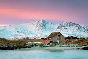 Snow Covered Prints: Old red wooden barn (rorbu) and snow-covered mountains beneath a pink sky at dawn