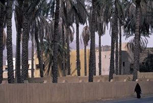 An Omani woman in traditional Arabic dress walks along the road