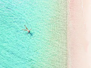 West Indies Prints: Overhead view of a woman sunbathing floating in the turquoise sea on a pink sand beach