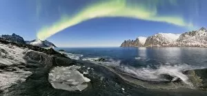 Panorama of frozen sea and rocky peaks illuminated by the Northern Lights Tungeneset