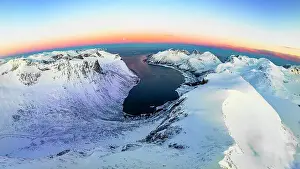 Panoramic aerial view of frozen fjord and majestic snowy mountains surrounding Bergsfjord at dawn, Senja, Troms county, Norway