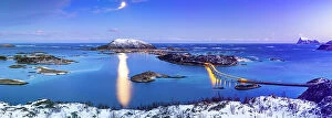 Drone Collection: Panoramic view of Sommaroy bridge along a frozen fjord lit by moon at dusk, Troms county, Norway