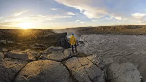 Admiring Gallery: a person enjoys the sunset near a Dettifoss waterfall, during a sunset with a midnight sun