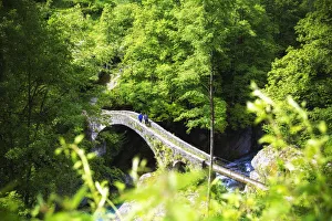Two persons walks on the Ponte della Merla(Merla Bridge). Maggia River, Brontallo