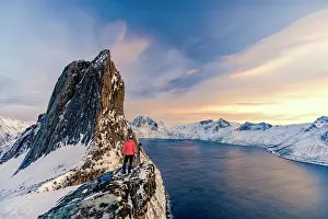 Majestic Prints: Photographer admiring Segla mountain peak covered with snow standing on top of rocks at sunset