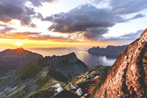 Photographer admiring the sun rays in the burning sky at sunset from Husfjellet mountain