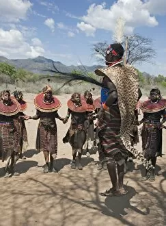 Pokot Women Collection: A Pokot warrior wearing a cheetah skin jumps high in the air surrounded by young women to